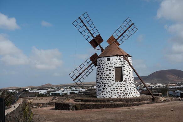 Weiß getünchte Windmühle mit braunen Holzflügeln auf Lanzarote bei leicht bewölktem Himmel.